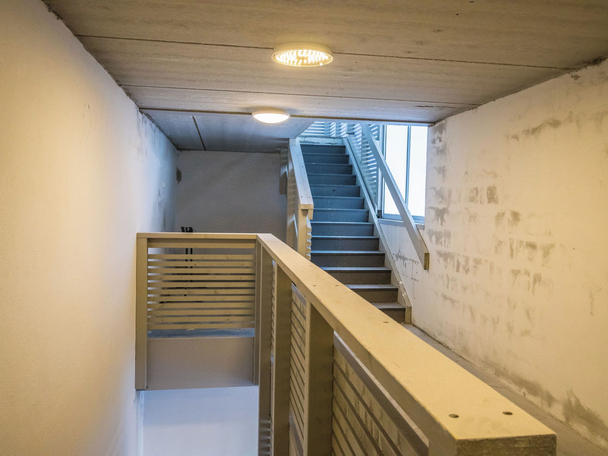 Un escalier avec une rampe en métal, des murs en béton et un luminaire au plafond.