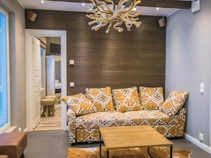 Een moderne woonkamer met een gestreept bankstel, een houten salontafel en een bijzondere plafondlamp.