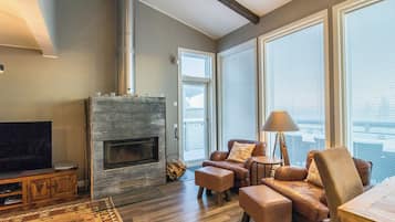 A modern living room with a fireplace, leather sofas, a TV, and large windows.