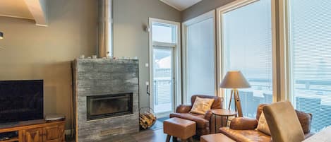 A modern living room with a fireplace, leather sofas, a TV, and large windows.