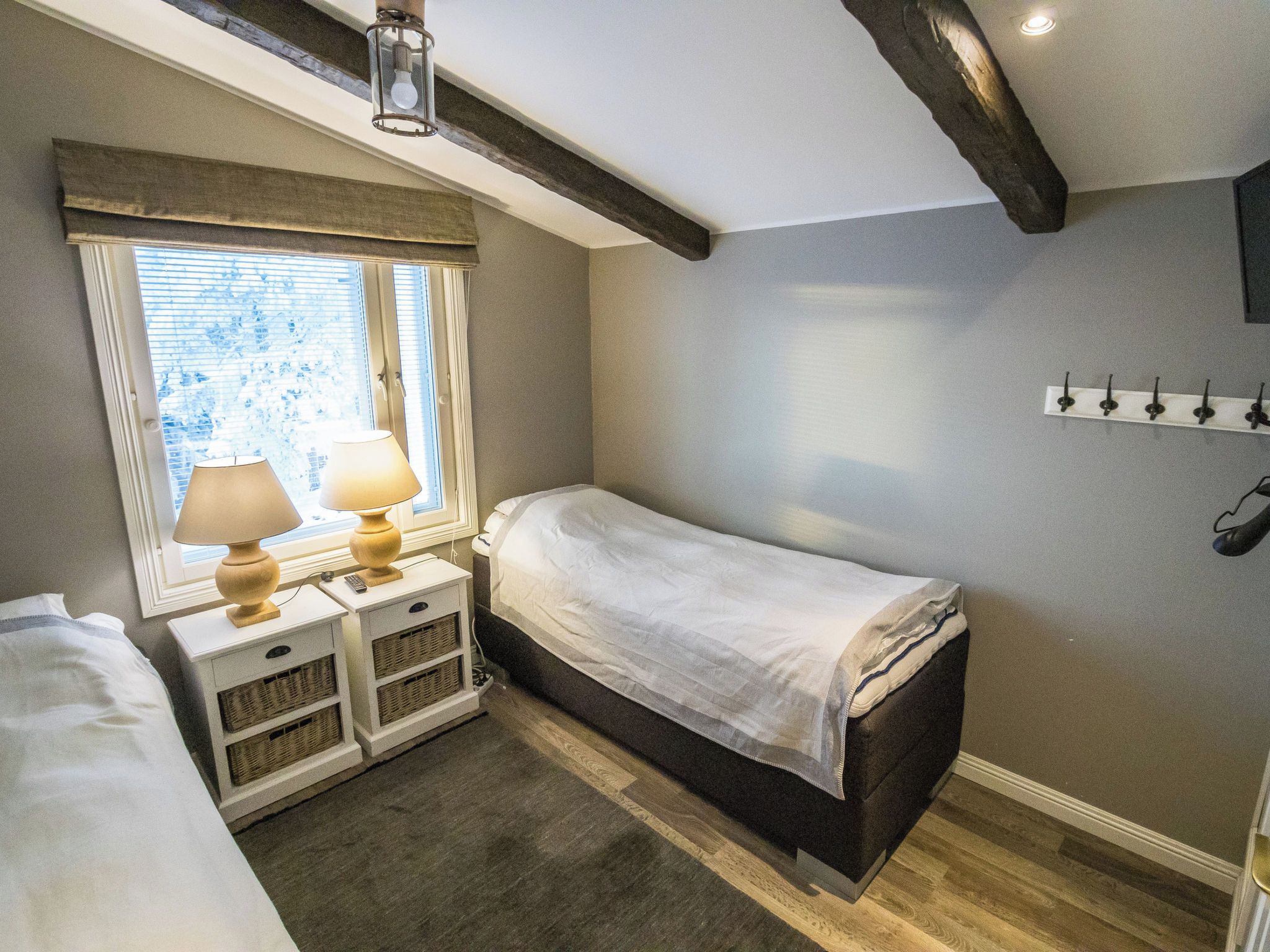 Un dormitorio con una cama individual, mesitas de noche, una lámpara, una ventana con persianas y un perchero.
