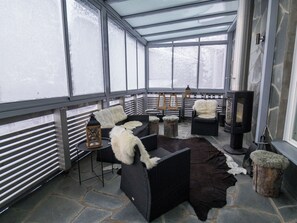 A covered outdoor seating area with stone flooring, wicker furniture, and a wood-burning stove.