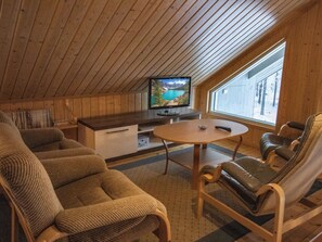 Una habitación acogedora con techo de madera, un televisor sobre un mueble de madera, una mesa redonda y dos sillones de cuero.