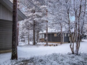 Ein verschneiter Wohnbereich mit einem Haus, einer Holzterrasse und einer Leiter, die zum zweiten Stock führt.