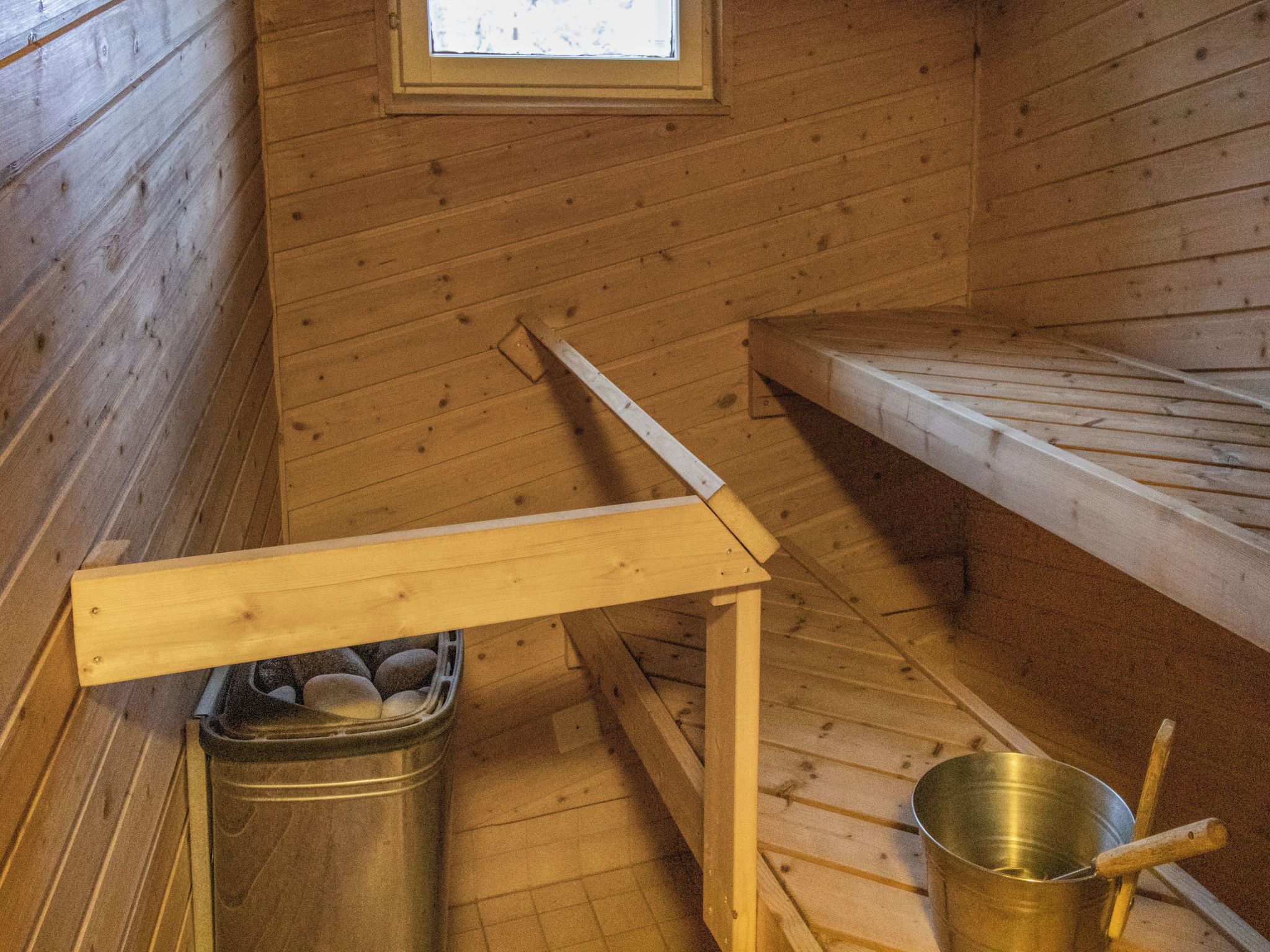 A wooden cabin interior with a metal bucket, a wooden table, and a window.