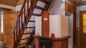 Una escalera que sube a un piso superior, una chimenea con un jarrón rojo y paredes de madera.