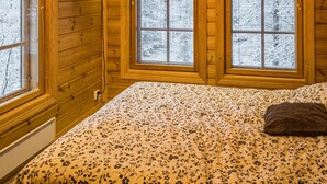 Habitación de cabaña de madera con una cama, televisión y ventanas amplias.