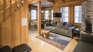 Interior de una cabaña de madera con sofá, televisor, chimenea y comedor.