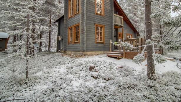 Una cabaña de troncos de dos pisos con un balcón, rodeada de árboles cubiertos de nieve.