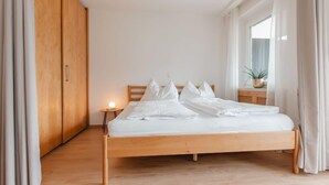 Un lit bien fait dans une pièce au plancher de bois, avec une armoire en bois et une table de chevet sur laquelle se trouve une lampe.