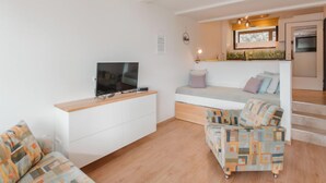 Un salon moderne avec un téléviseur à écran plat, un canapé blanc, un fauteuil à motifs et un banc en bois.