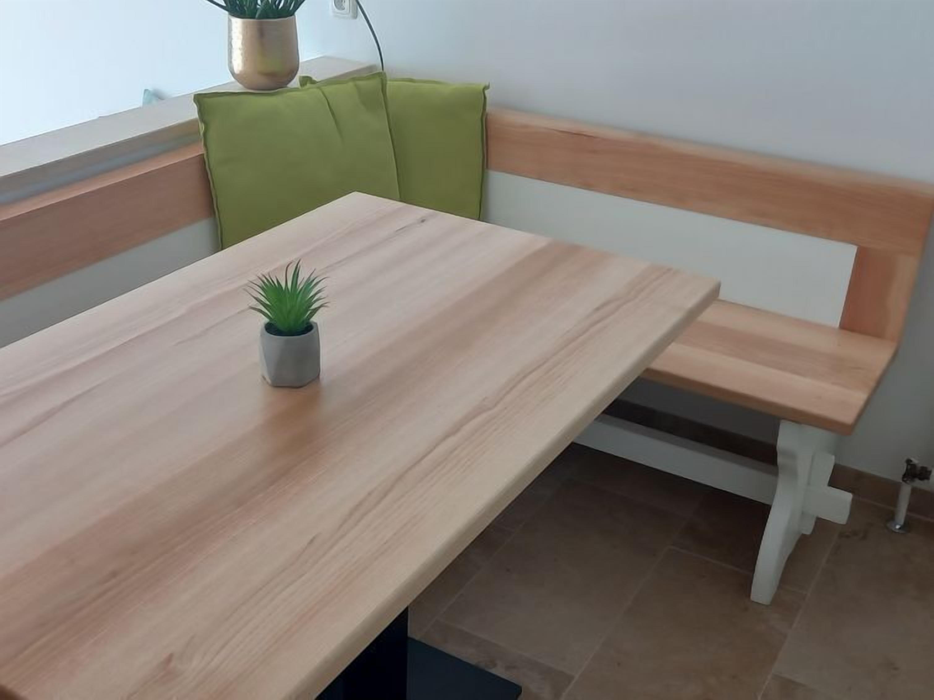 Een houten tafel met een kleine plant in pot, een groene met kussens beklede bank en een witte hoofdeinde tegen een muur.