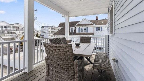 A covered outdoor balcony with wicker furniture, a table, and a view of neighboring houses. - 2 Bedroom Condo Only Steps to the Beach! (North Wildwood)