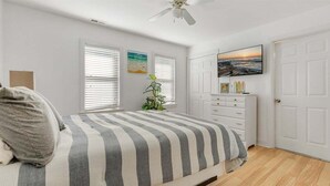 A bedroom with a bed, a dresser, a plant, and a painting on the wall. - 2 Bedroom Condo Only Steps to the Beach! (North Wildwood)