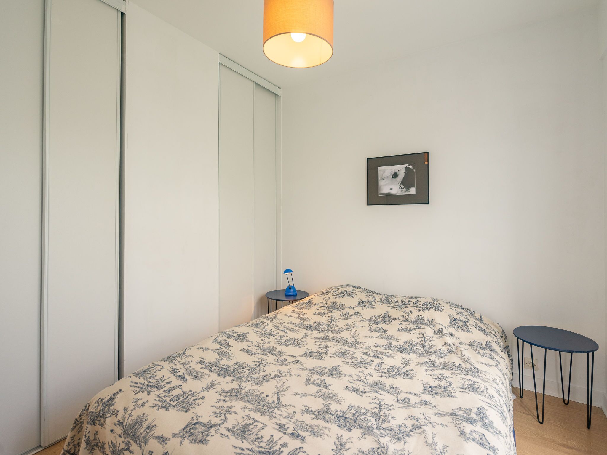 Une chambre à coucher avec un lit, une petite table, une lampe, un tableau au mur et une armoire.