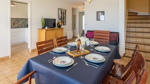 Ein Essbereich mit einem Tisch für sechs Personen, eine Küche im Hintergrund und eine Treppe zur Rechten.