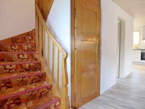 Un escalier recouvert d’une moquette à motifs floraux, une porte en bois et, au fond, un coin cuisine.