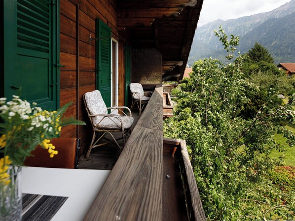 A wooden cabin with a balcony, two wicker chairs, and a table.