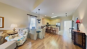 Un'ampia zona giorno con divano, poltrona e tavolo da pranzo. Si intravede in secondo piano una cucina con elettrodomestici moderni.