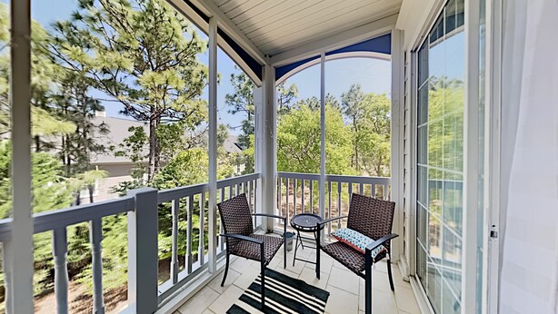 Un balcone coperto con due poltrone in vimini e un tavolino, con vista su un paesaggio verde con alberi e un edificio sullo sfondo.