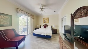 Una camera da letto con un letto, una sedia, una TV e una ventola a soffitto.