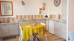A compact kitchen with a dining table, a microwave, a refrigerator, and a colorful striped backsplash. - PALMIER *** studio with garden and parking (Le Bois-Plage-en-Ré)
