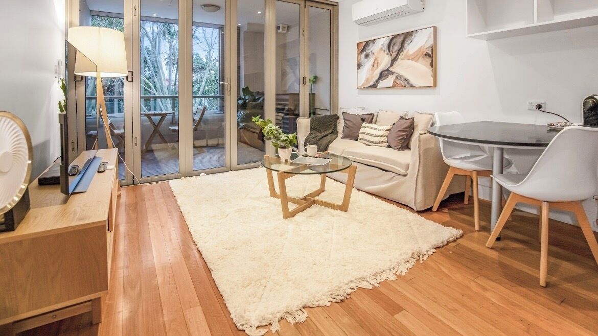 A modern living room with a glass table, a sofa, a coffee table, and a view through glass doors to an outdoor area.