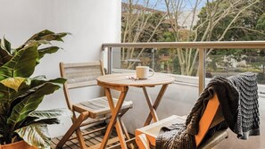 Ein Balkon mit Tisch und zwei Stühlen, einem Blumentopf und Blick auf Häuser und Bäume.