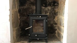 A black wood-burning stove with a glass door, set in a stone-walled alcove. - Beachfront Apartment With Woodburner & Courtyard (St Leonards-On-Sea)