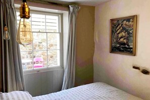 Un dormitorio con cama, ventana con cortinas, un cuadro en la pared y una lámpara colgante.