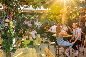 An outdoor seating area with wooden tables and benches, surrounded by lush greenery and hanging plants. - Charming Luxury Holiday Stay in Beautful Location (London)