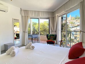 A hotel room with a large bed, a balcony with a chair, and a view of the city.