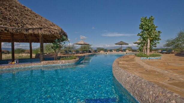 Una piscina con agua azul cristalina, rodeada de muros de piedra y protegida por sombrillas de paja.