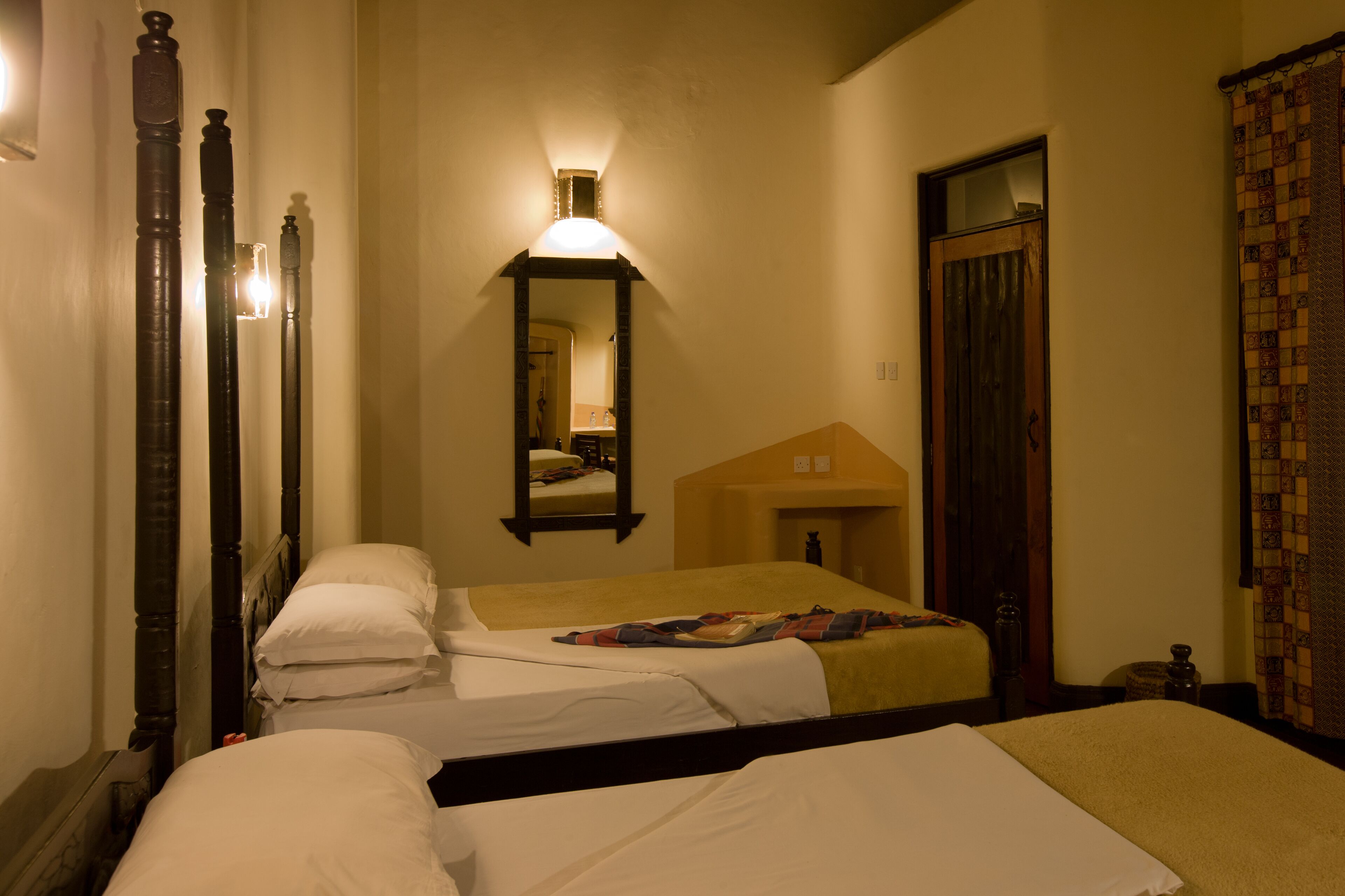 A hotel room with two beds, a mirror, a wall-mounted light, and a door.