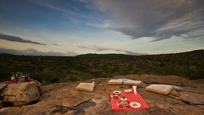 Un montaje para picnic sobre un afloramiento rocoso, con un mantel a cuadros rojos, botellas y vasos sobre la roca.