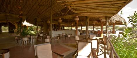 An open-air dining area with wooden furniture and a thatched roof.