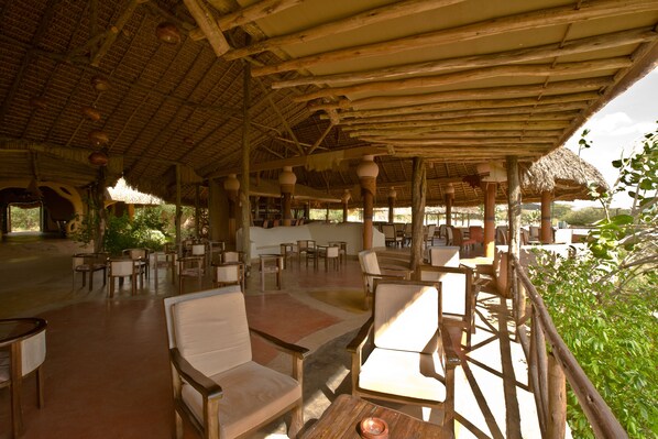 An open-air dining area with wooden furniture and a thatched roof.