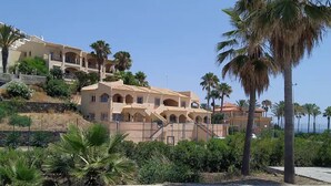 Ein mehrgeschossiges Hotel im mediterranen Stil, mit Balkonen und einem angelegten Garten mit Palmen.