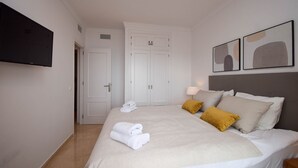 Ein Hotelzimmer mit Bett, weißen Vorhängen, einem Flachbildfernseher und einem Bild an der Wand.