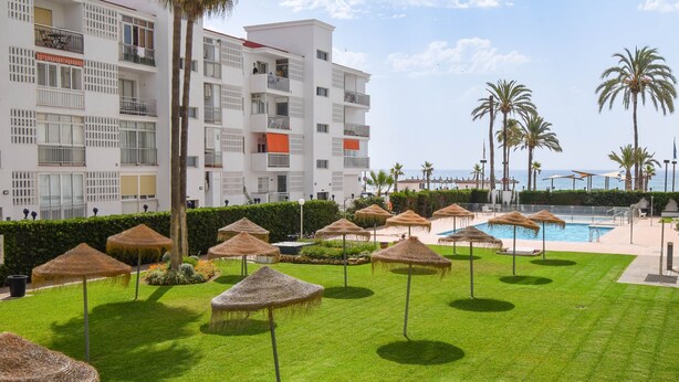 Ein Hotel mit Swimmingpool, Reetdachschirmen und Palmen.