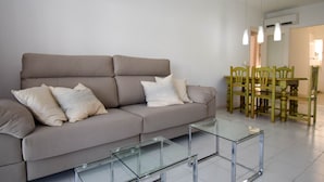 Ein Wohnzimmer mit einer Couch, zwei Glastischen und einem Essbereich mit Holztischen und -stühlen.