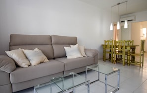 A living room with a sofa, two glass coffee tables, and a dining area with wooden chairs and a table.