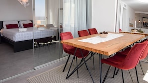 A modern bedroom with a large bed, a glass partition, a wooden dining table with red chairs, and a kitchen visible through an open door. - Ref: 307 Modern beachfront apartment in Torreblanca with stunning sea views (Fuengirola)