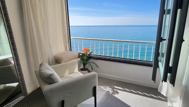 A balcony with a view of the ocean, a chair, a small table with a plant, and a window with curtains. - Ref: 307 Modern beachfront apartment in Torreblanca with stunning sea views (Fuengirola)
