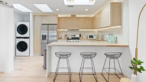 A modern kitchen with a central island, bar stools, a built-in washing machine, and a refrigerator.
