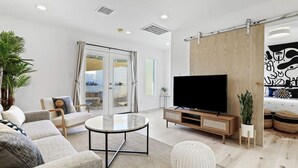 A modern living room with a flat-screen TV, a round coffee table, and a sliding glass door leading to an outdoor area.