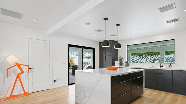 A modern kitchen with a marble island, black cabinets, and pendant lighting.