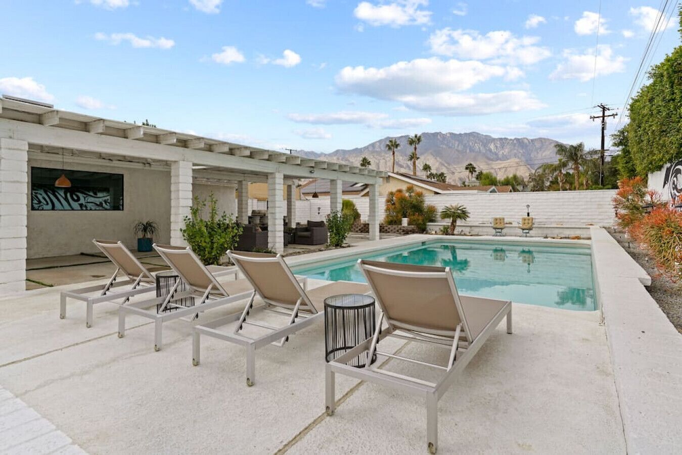Un espace piscine avec des chaises longues, un coin salon abrité et une vue sur les montagnes en arrière-plan.