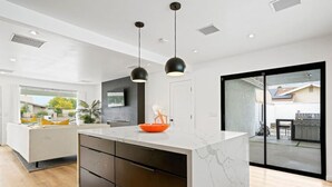 A modern kitchen with a marble island, black pendant lights, and a view to the backyard.