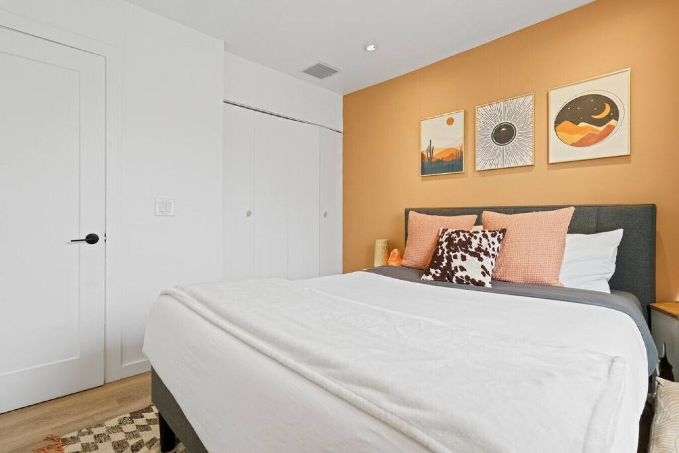A bedroom with a bed, a wardrobe, and three wall-mounted pictures.